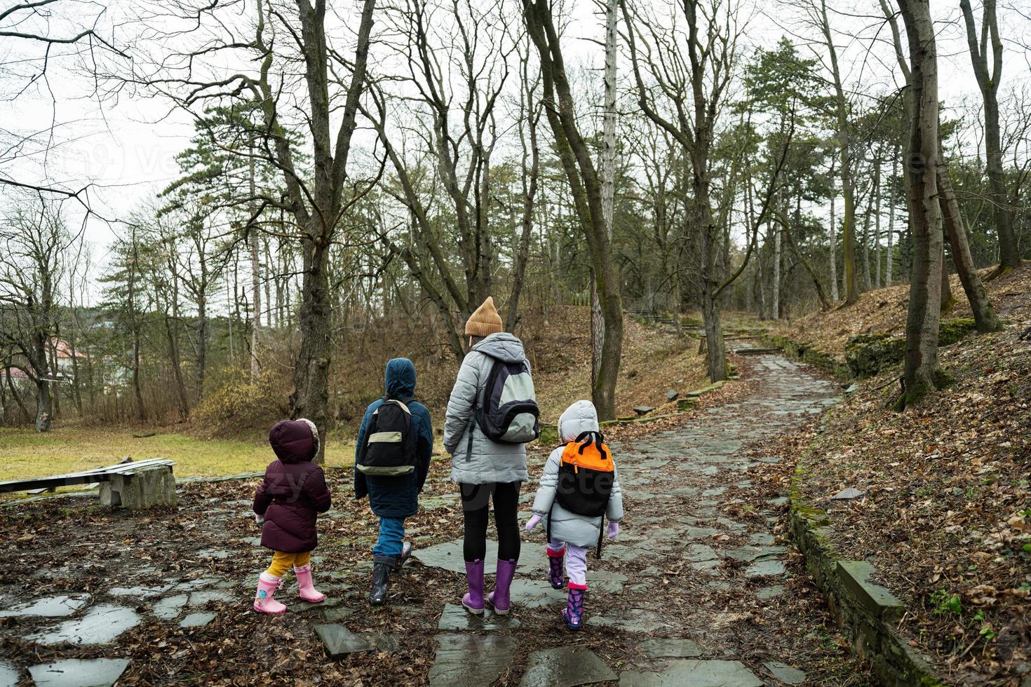 indietro di mamma e bambini con zaini a piedi lungo il foresta pietra strada dopo pioggia insieme. foto