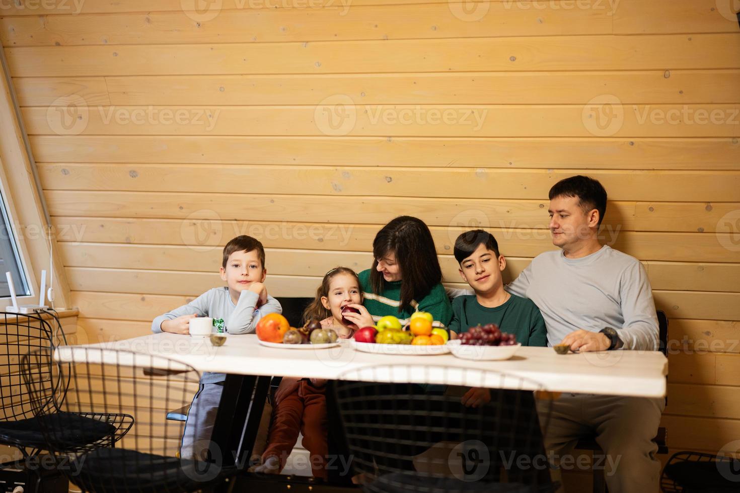 famiglia con tre bambini mangiare frutta nel di legno nazione Casa su fine settimana. foto