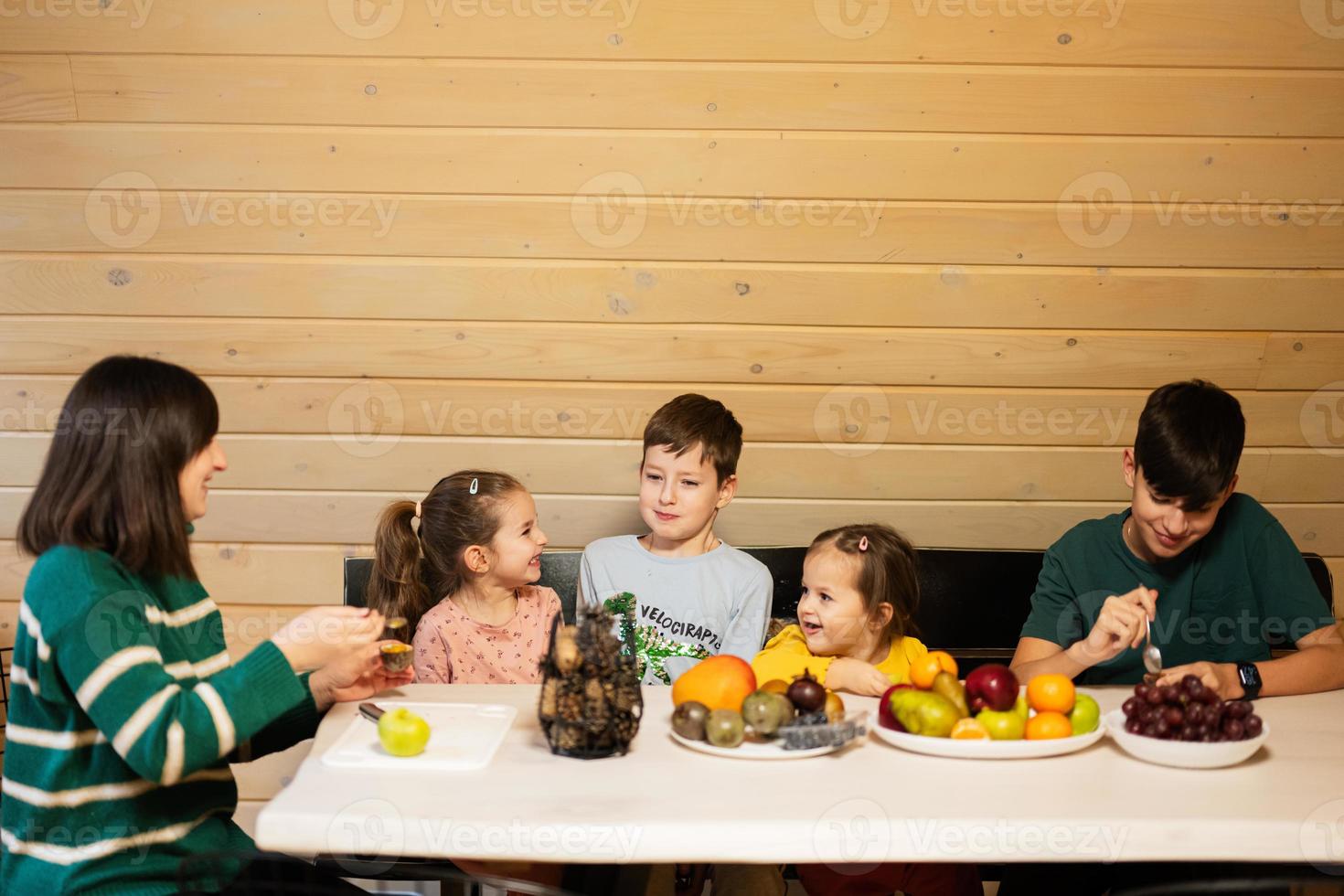 madre con quattro bambini mangiare frutta nel di legno nazione Casa su fine settimana. foto
