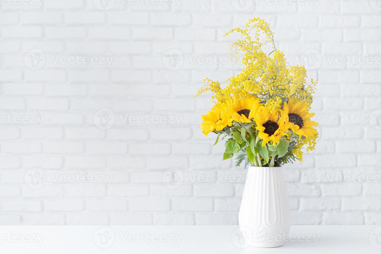 fiorire di mimosa e girasoli nel bianca ceramica vaso su bianca mattone parete sfondo con spazio per testo foto