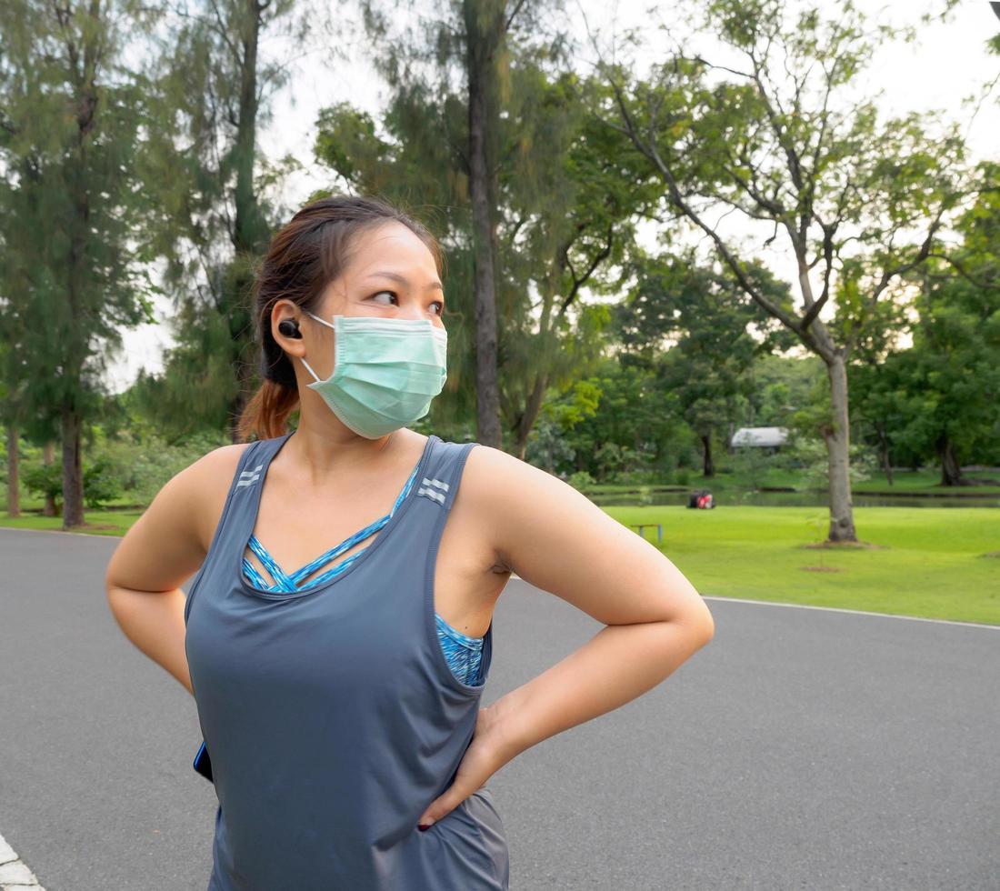 ritratto di un' bellissimo asiatico donna nel abbigliamento sportivo, in piedi con sua Indietro, allungamento prima esercizio all'aperto nel il parco nel il mattina per raggiungere un' salutare stile di vita. salutare riscaldamento su foto