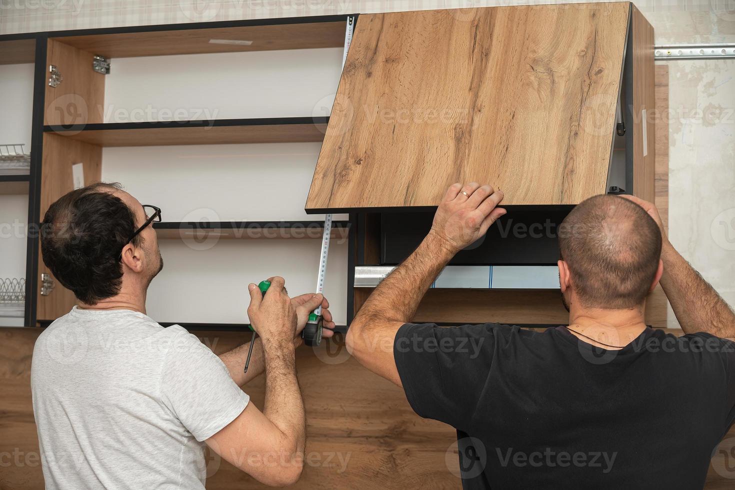 Due artigiani, mobilia creatori e assemblatori, siamo installazione un' moderno cucina nel un' casa, utensili nel loro mani. concetto mobilia per ordine, miglioramento di vivente condizioni, riparazione foto