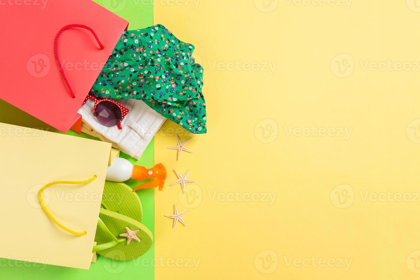 estate concetto di colorato shopping borse pieno di Abiti. regalo borse con maglietta, denim corti, Flip flop e bottiglia di crema solare. estate Lista dei desideri concetto. superiore Visualizza copia spazio su giallo sfondo foto