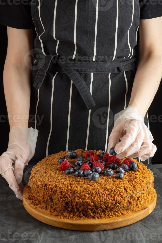 un' femmina capocuoco decora un' fatti in casa carota torta con fresco frutti di bosco su un' buio sfondo foto