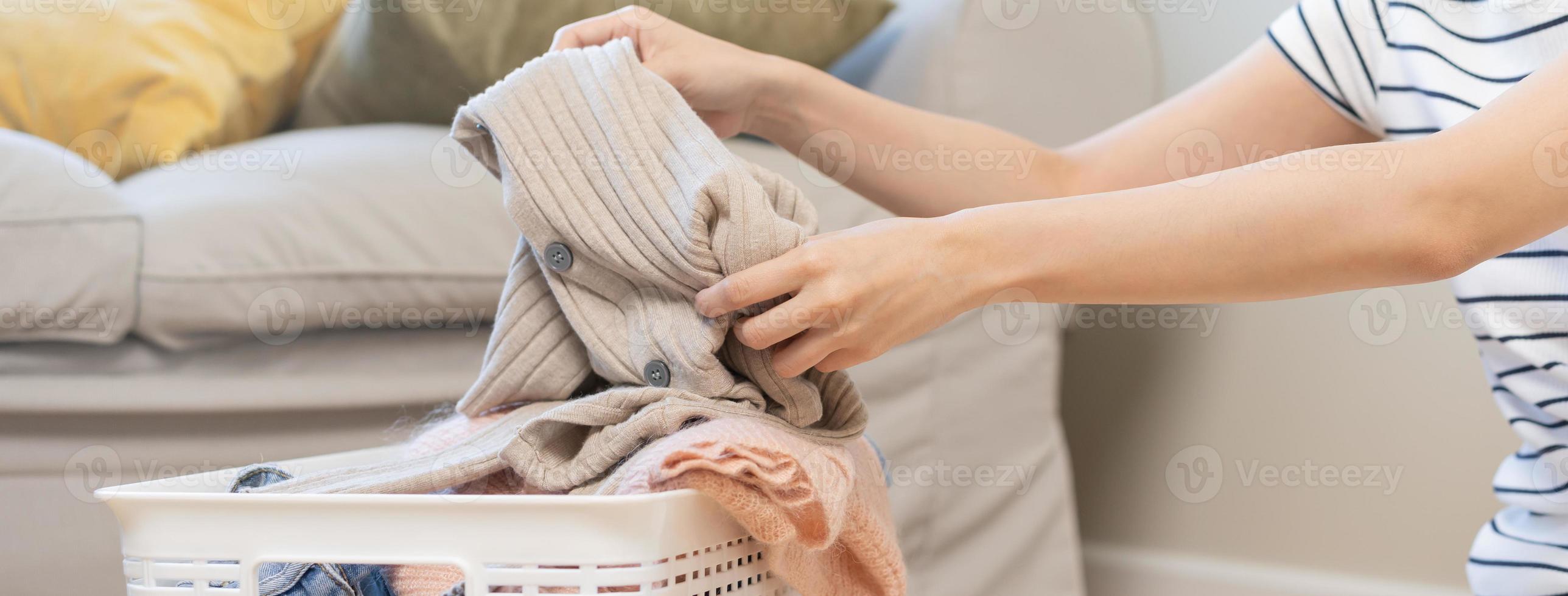 casalinga, vicino su mano nel asiatico giovane donna prendere su il lavaggio pulito Abiti a partire dal il cestino per piegare esso nel dopo esso ha essiccato. domestica Lavorando nel camera a casa. lavanderia e pulizia di lavoretto. foto