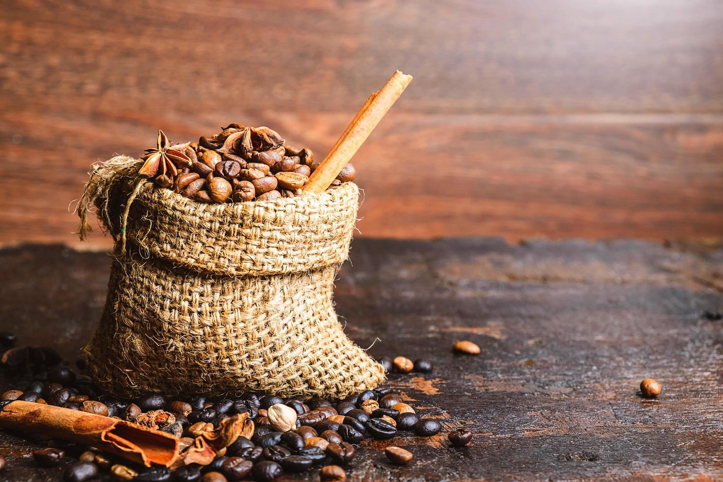 chicchi di caffè e bastoncini di cannella in un sacchetto di tela ruvida su un tavolo di legno scuro foto