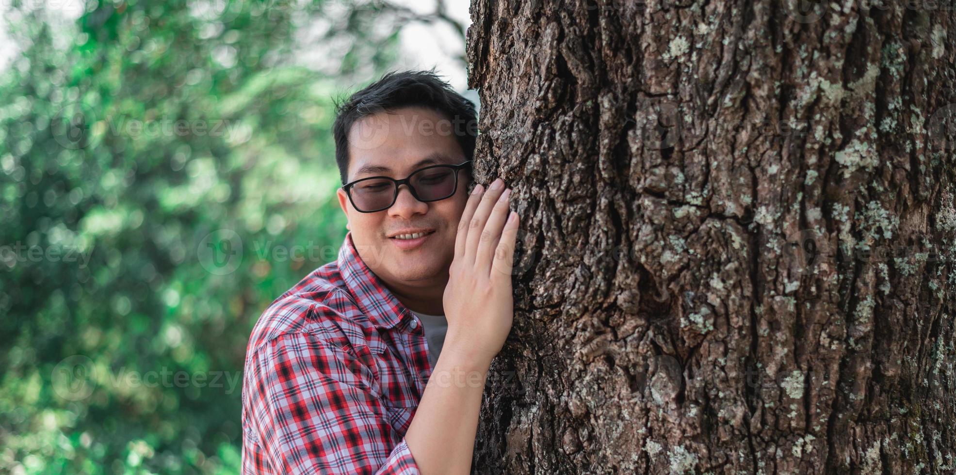 ritratto di contento asiatico uomo abbracciare un' albero nel foresta foto