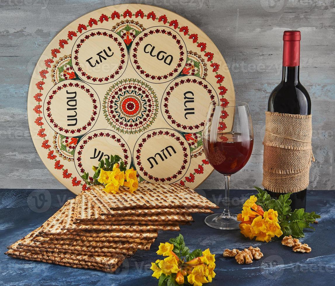 Pesach celebrazione concetto - ebraico vacanza pesach. sfondo con giallo fiori con bicchiere di vino, matzah e piatto di seder su blu sfondo. tradizionale ebraico iscrizioni su piatto. foto