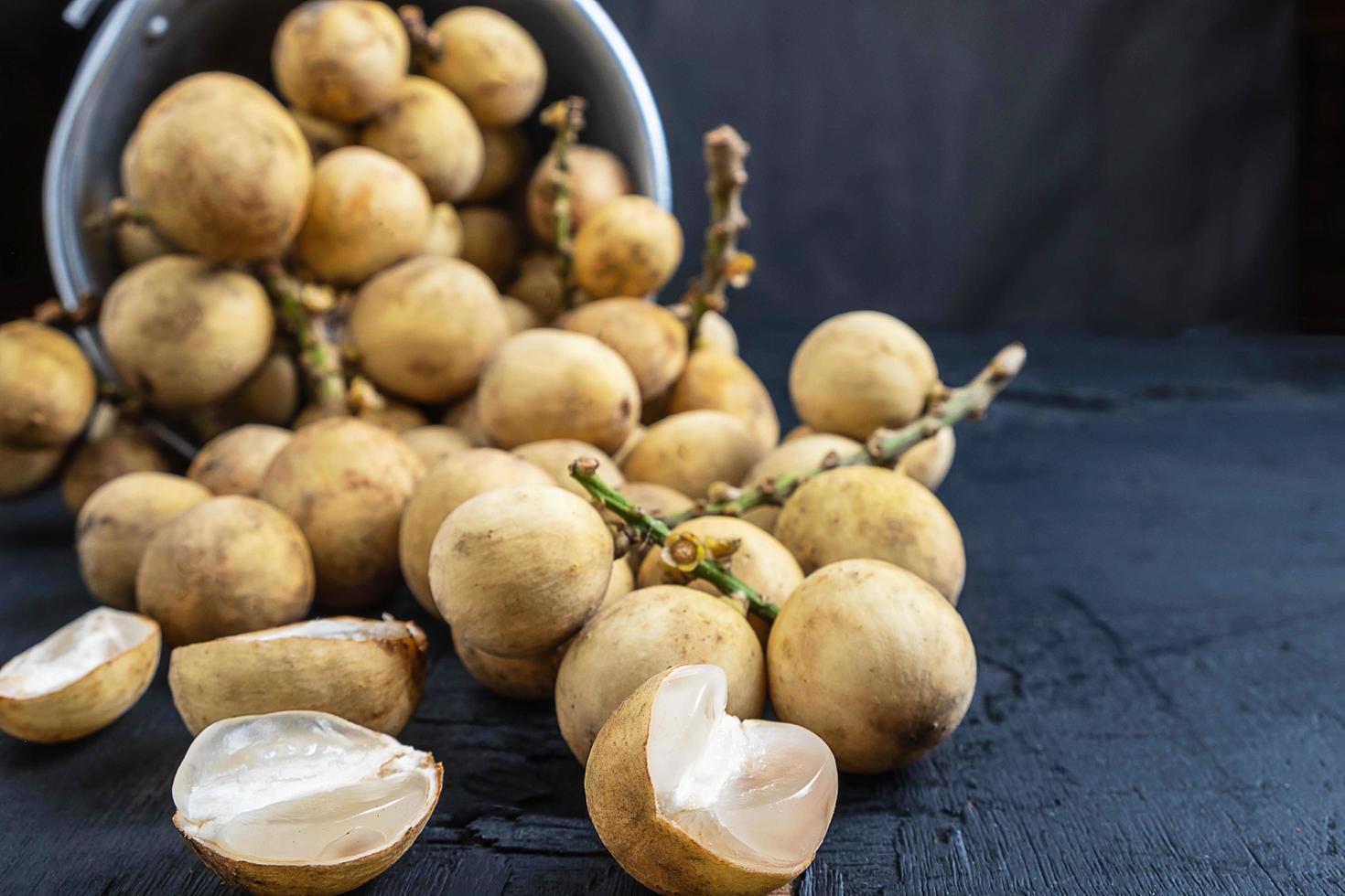 longkong o langsat frutta fuoriuscita di un secchio di metallo su uno sfondo di legno nero foto