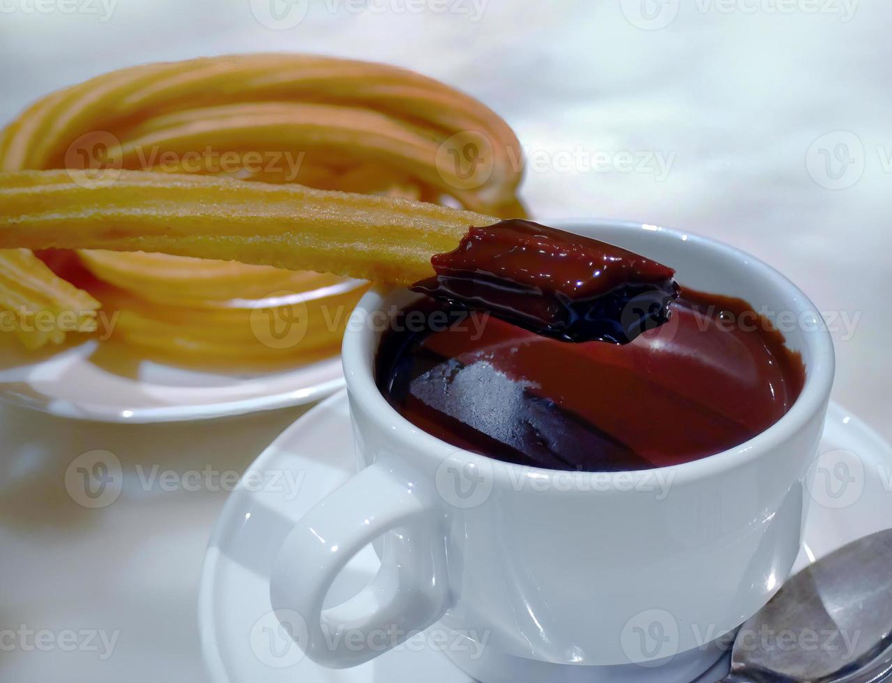 churros bastone immerso con cioccolato pronto per mangiare, su caldo di spessore cioccolato salsa nel bianca tazza, caffè negozio, famoso spagnolo prima colazione foto