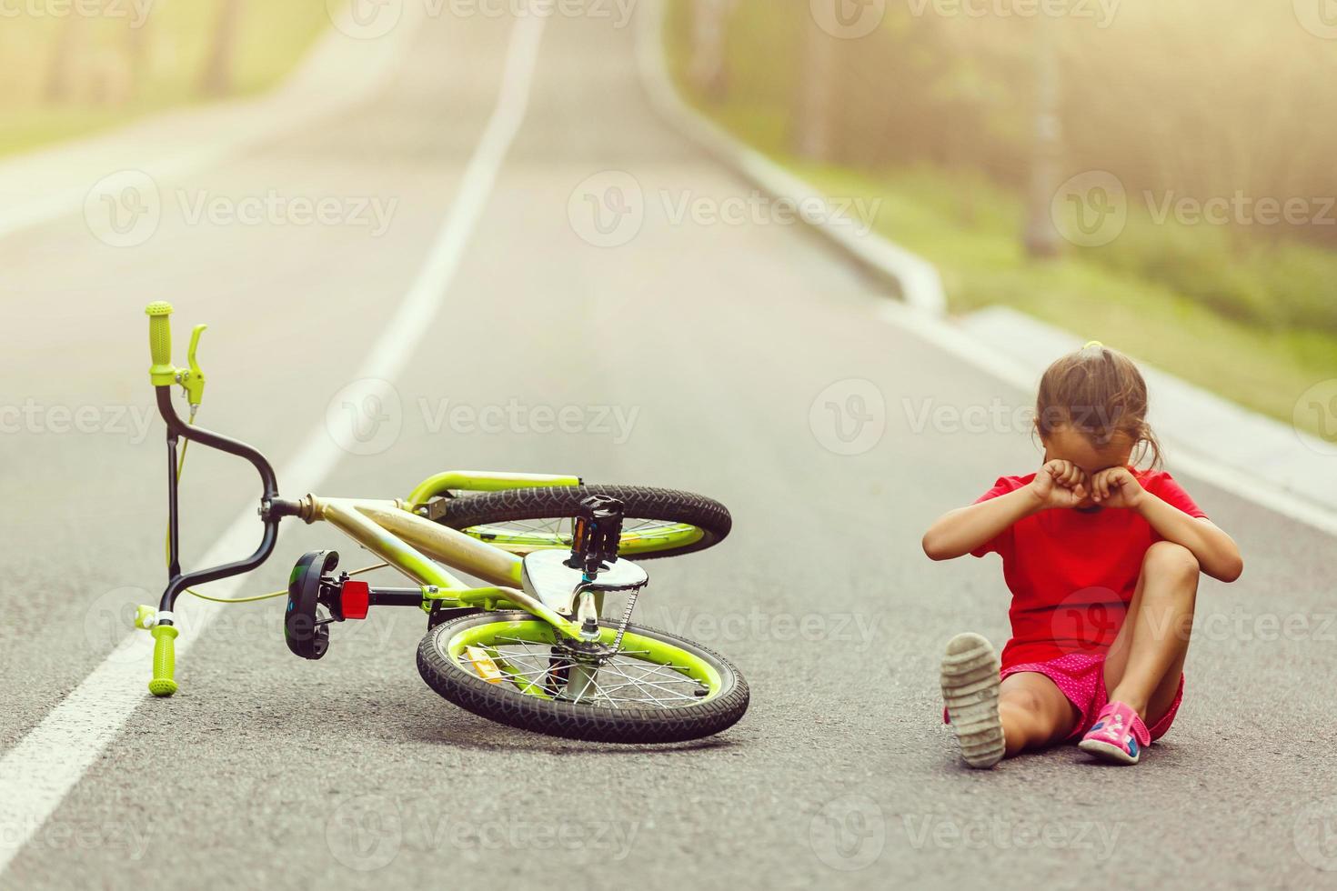 un' poco ragazza equitazione un' bicicletta. il bicicletta incidente. sedersi pianto su il strada foto