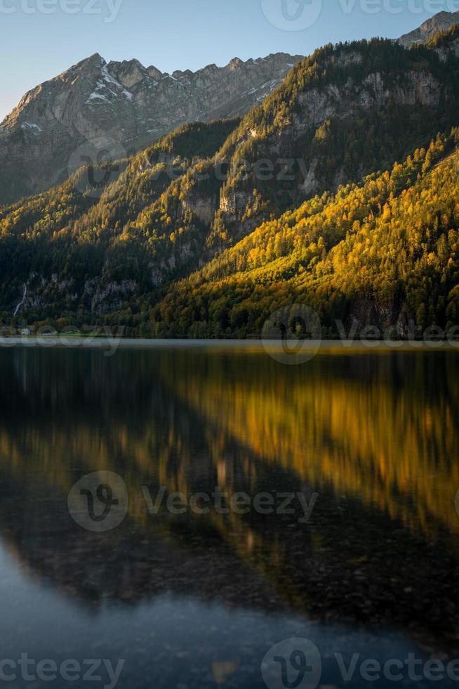 un' lago nel autunno riflettendo il montagne e il luce di il sole foto