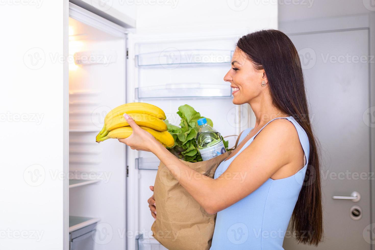 salutare mangiare concetto. dieta. bellissimo giovane donna vicino il frigo con salutare cibo. frutta e verdure nel il frigorifero. vegano cibo foto