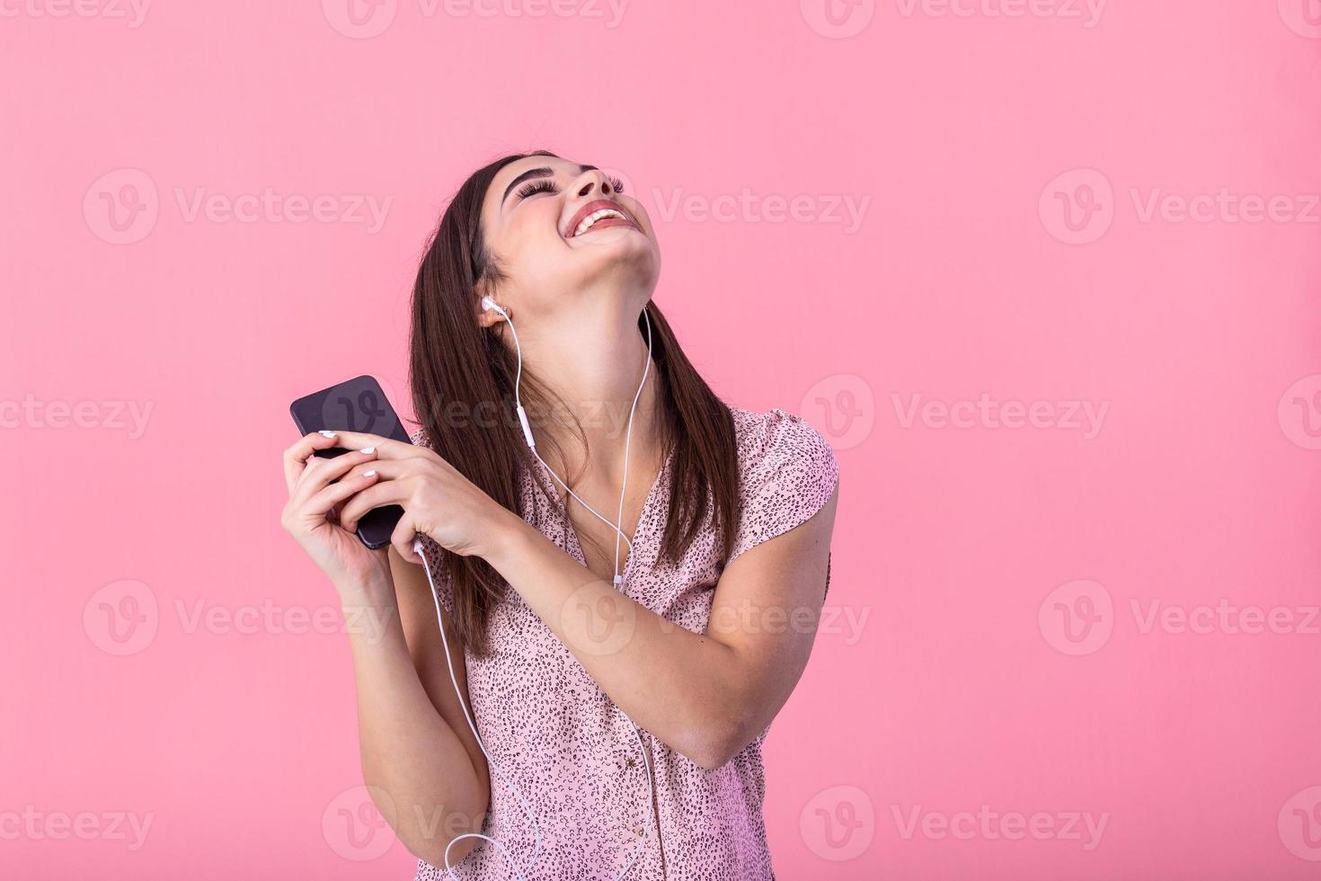 stile di vita concetto - ritratto di bellissimo donna gioioso ascoltando per musica con testa telefoni su mobile Telefono. rosa pastello studio sfondo. copia spazio. foto