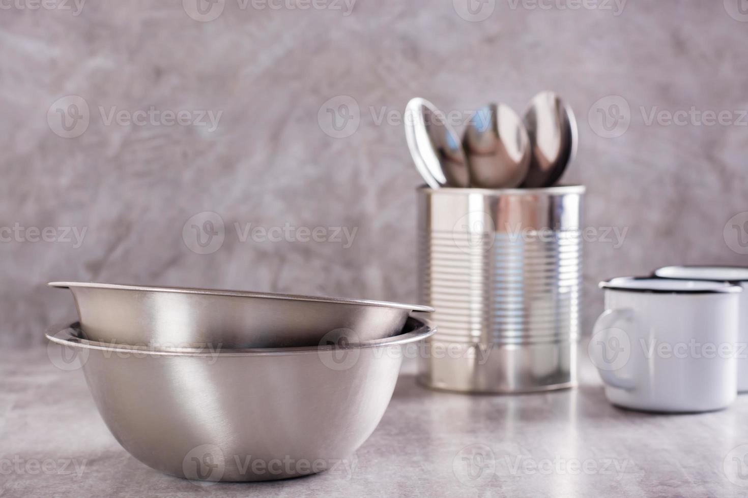 Due vuoto metallo ciotole, cucchiai nel un' può e metallo smalto tazze su un' grigio sfondo foto