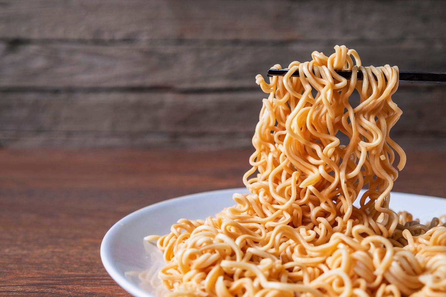 paio di bacchette raccogliendo spaghetti istantanei su un piatto bianco su un tavolo di legno foto