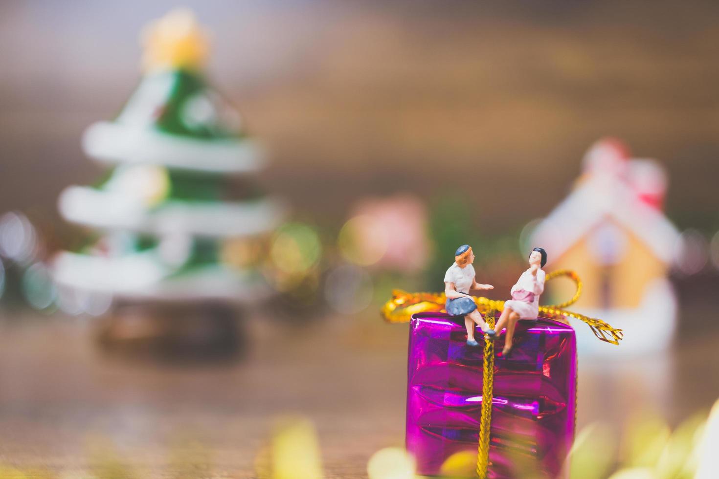 persone in miniatura su una confezione regalo con decorazioni natalizie in background foto