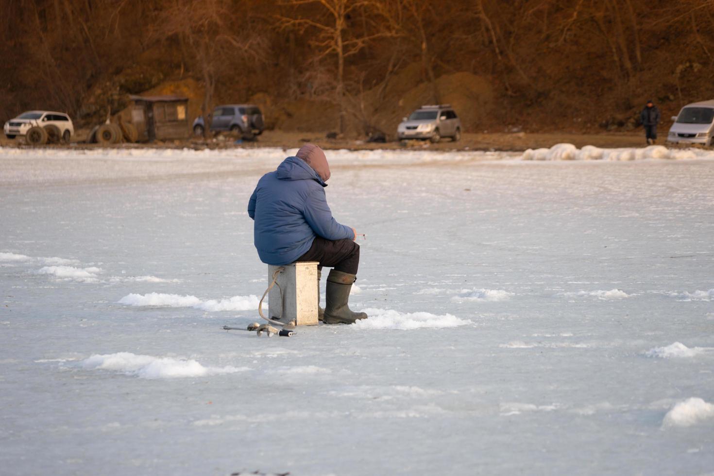 persona che pesca sul ghiaccio con le auto in background a vladivostok, russia foto