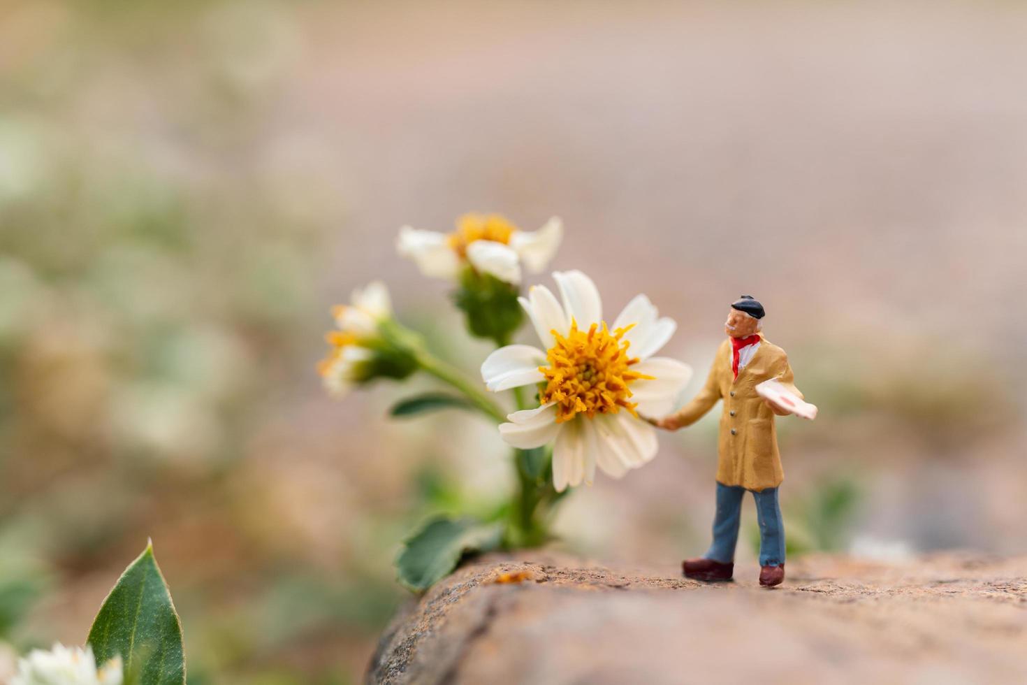 artista in miniatura che tiene un pennello e dipinge fiori in giardino foto