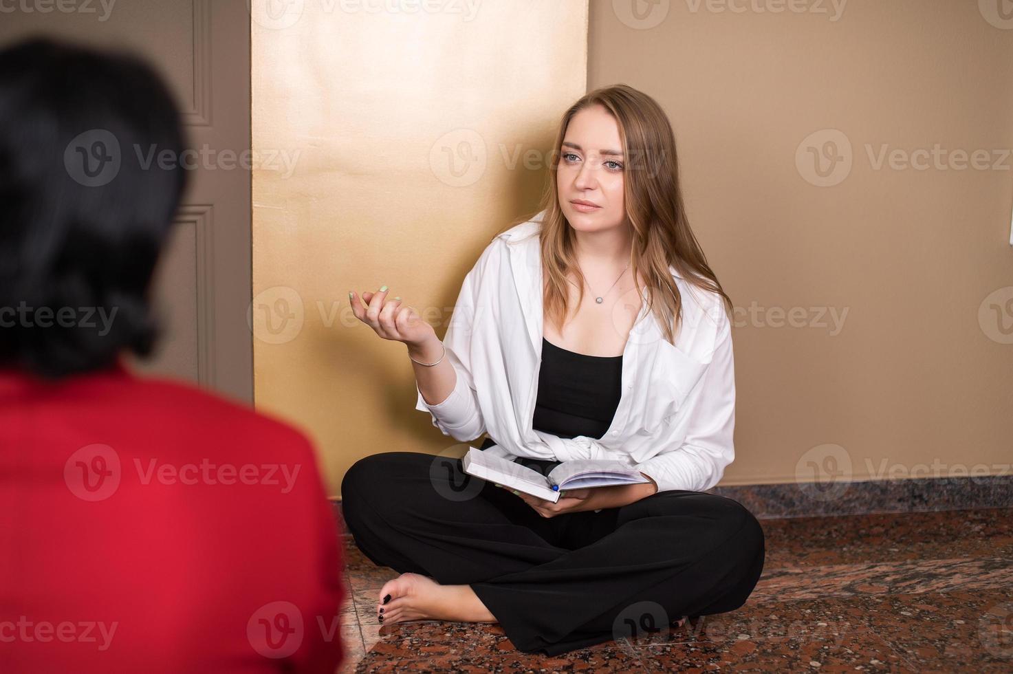 un' simpatico ragazza psicologo è ricevente un' cliente seduta su il pavimento con un' diario foto
