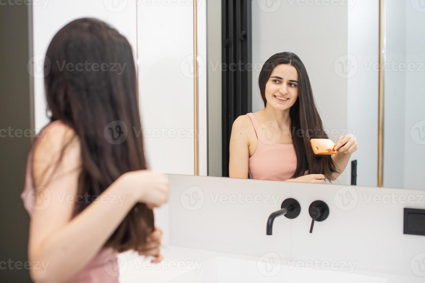 carino ragazza è in piedi nel il bagno e pettinatura sua lungo capelli foto