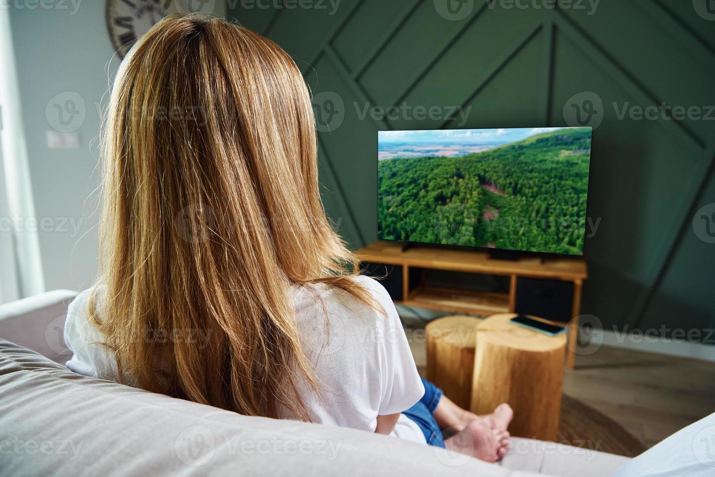 donna interruttore canali su tv impostato con a distanza controllo. foto