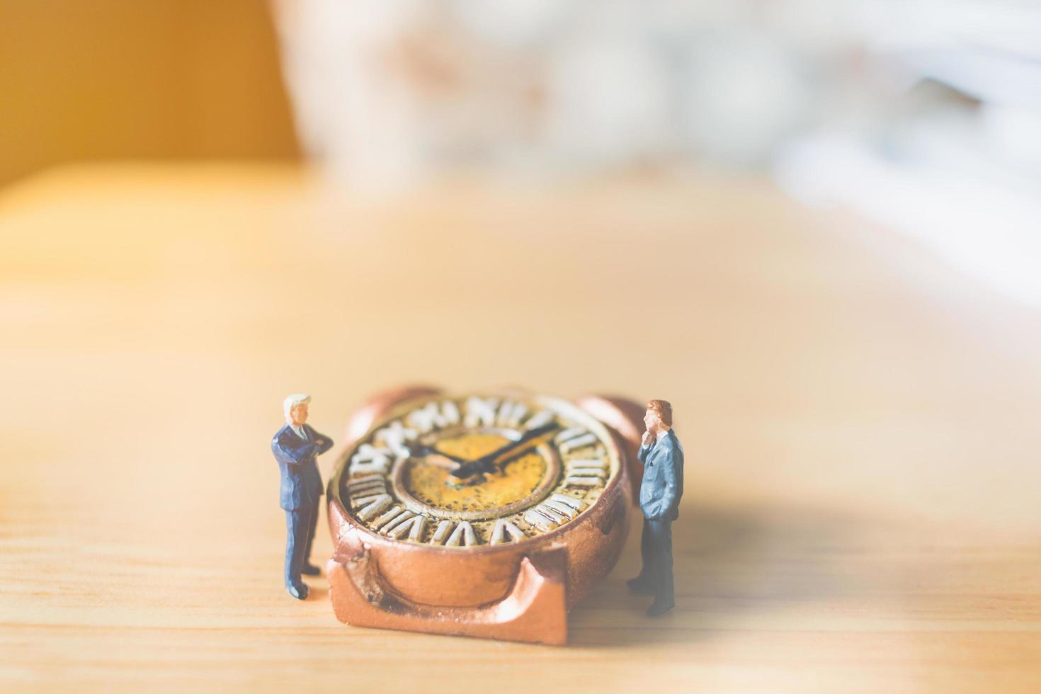 uomini d'affari in miniatura in piedi con un vecchio orologio su uno sfondo di legno foto