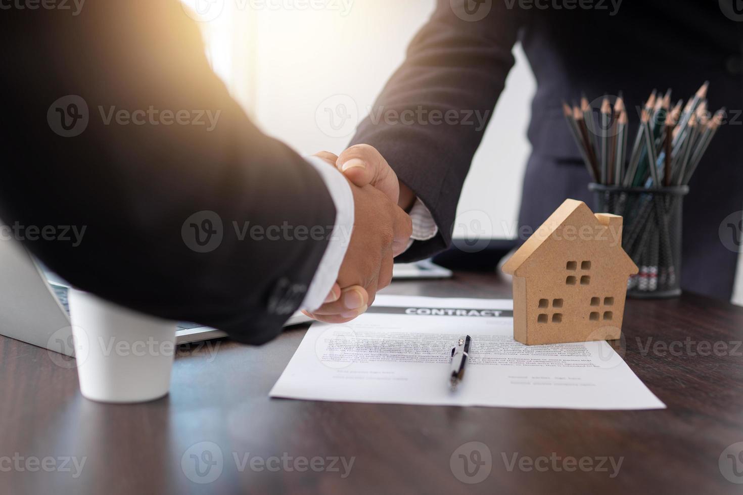Close up di uomini d'affari si stringono la mano sulla scrivania con il contratto e il modello di casa foto