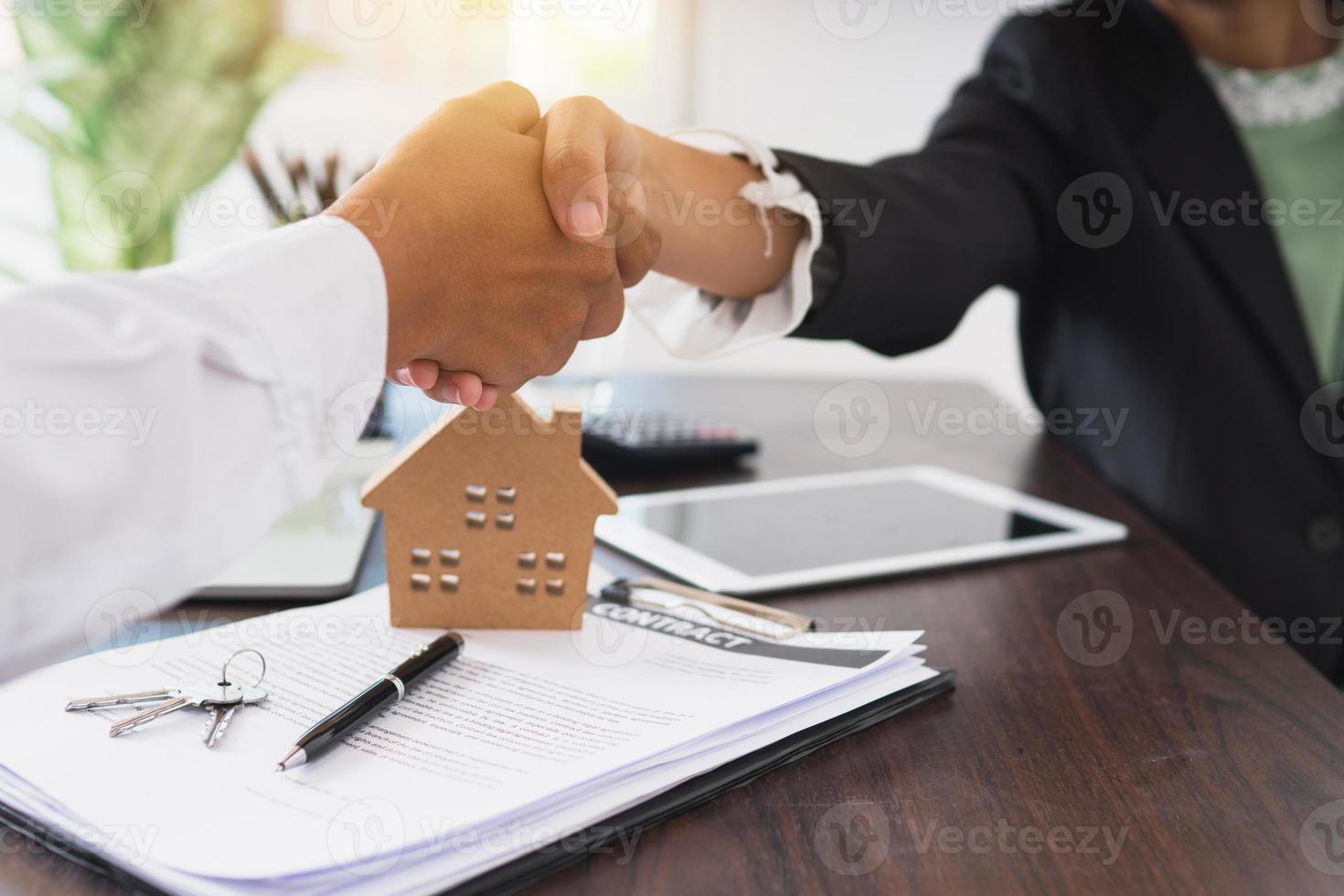 Close up di imprenditrice e uomo stringe la mano sulla scrivania con il contratto e il modello di casa foto