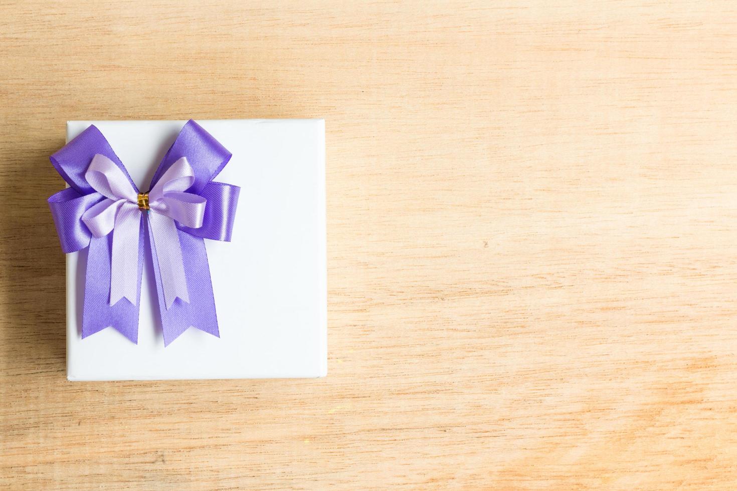fiocco di nastro viola su una confezione regalo bianca su uno sfondo di legno foto