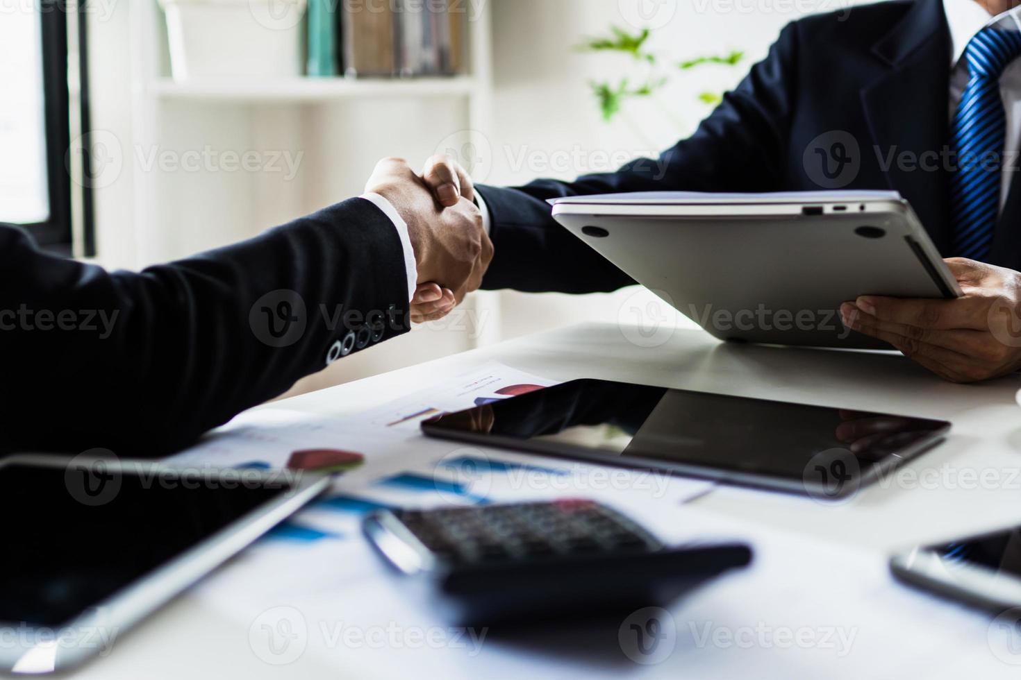due persone si stringono la mano su carte di tabelle e grafici accanto alle tavolette foto