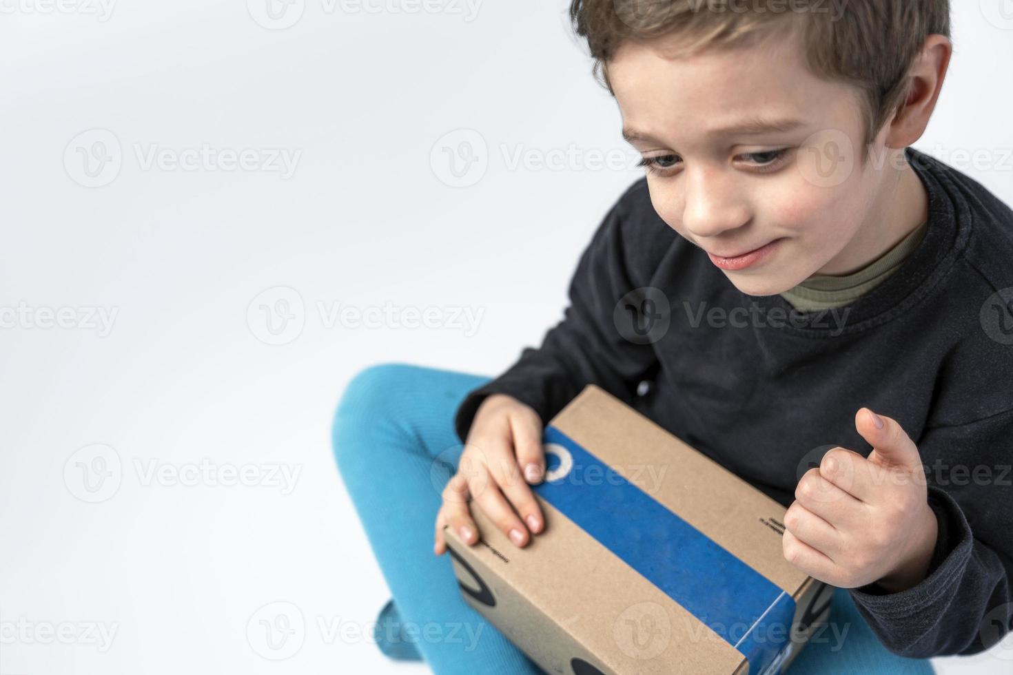 il bambino detiene un' cartone scatola con un' regalo inviato di il consegna servizio. foto