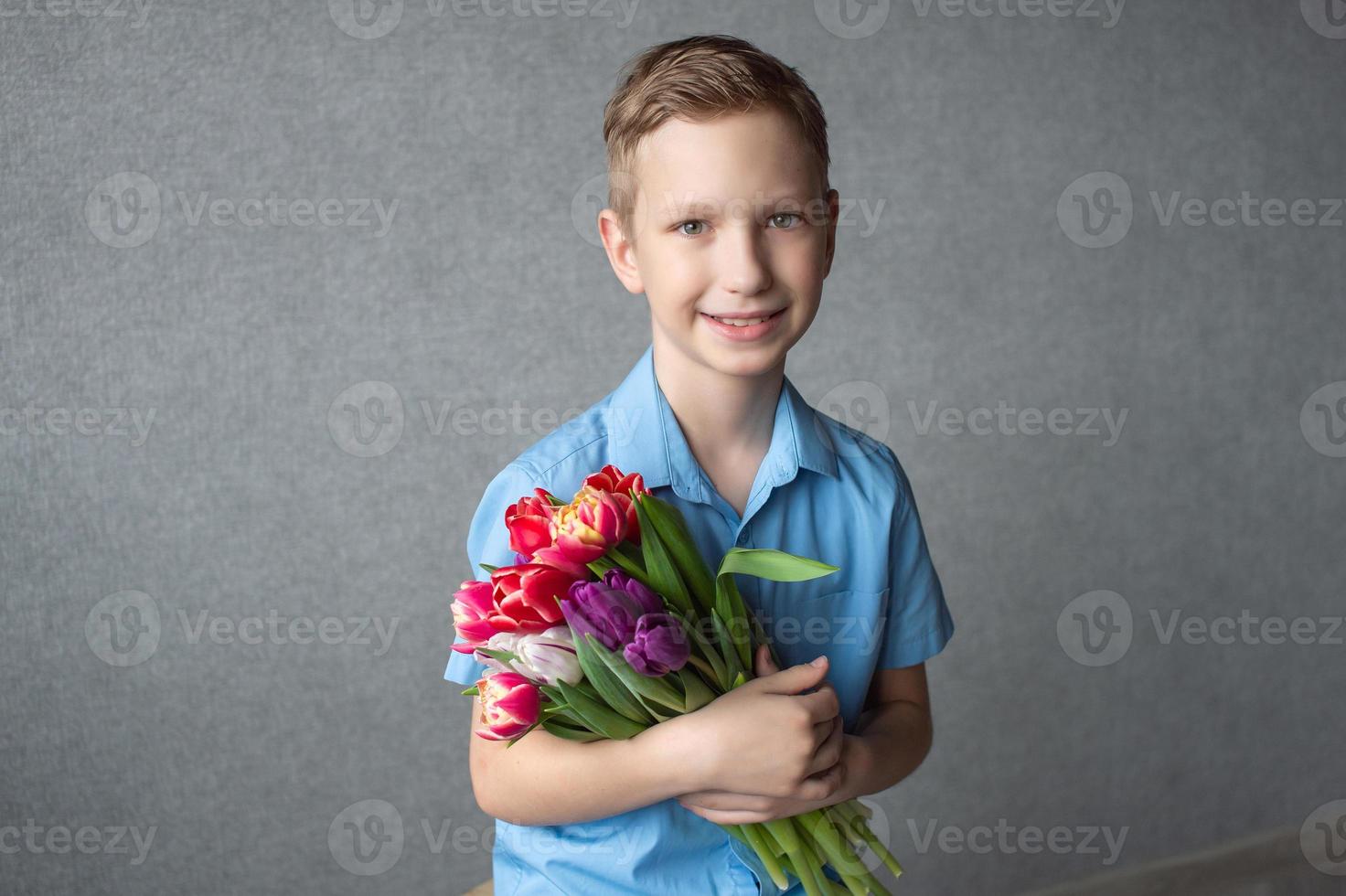 un' carino ragazzo nel un' camicia detiene un' colorato mazzo di tulipani nel il suo mani. spazio per testo foto