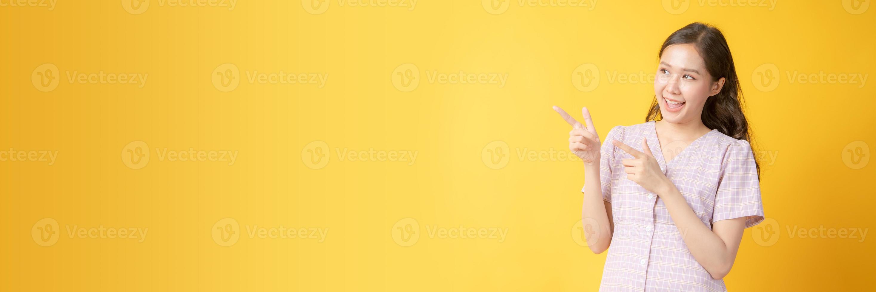 donna asiatica sorridente e gesticolando verso lo spazio della copia su sfondo giallo foto