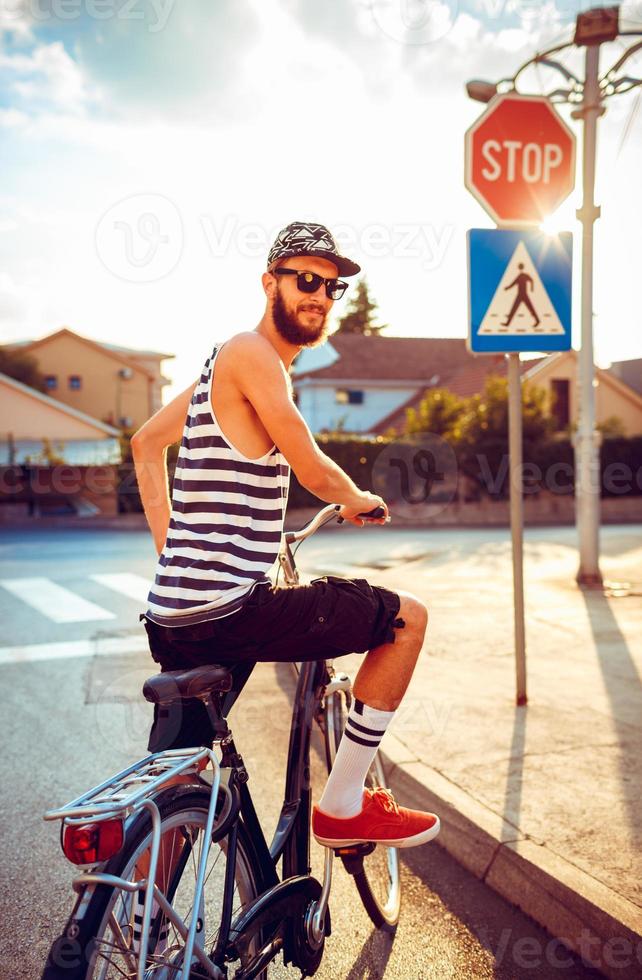 uomo nel occhiali da sole equitazione un' bicicletta su un' città strada a tramonto leggero foto