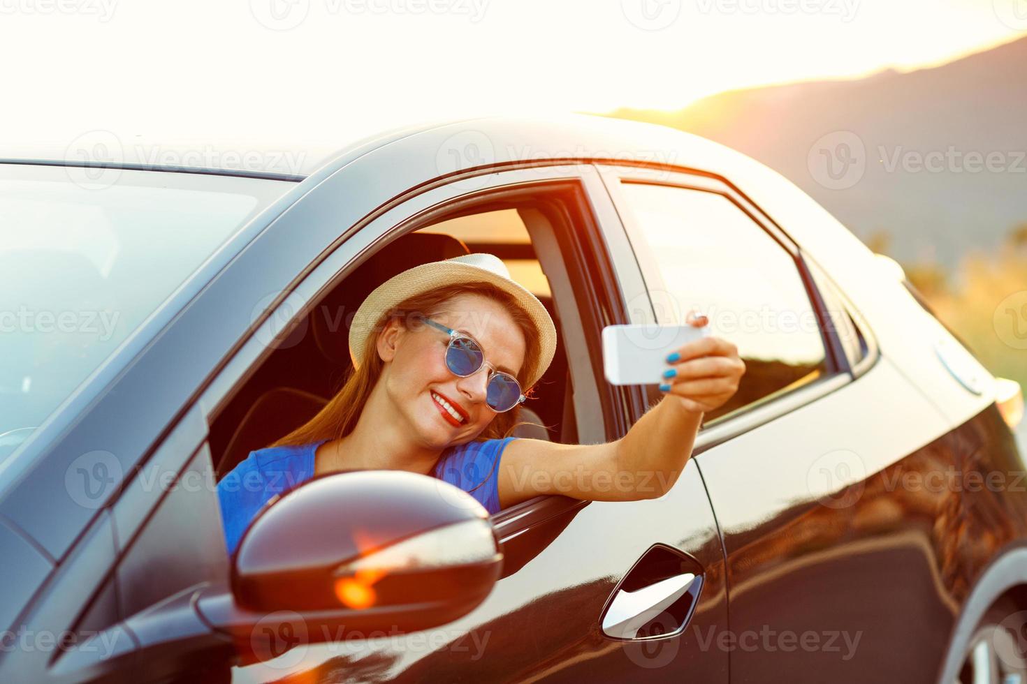 donna nel cappello e occhiali da sole fabbricazione se stesso ritratto seduta nel il auto foto