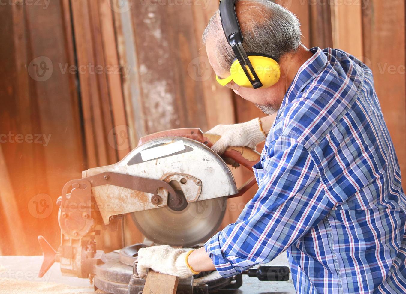 L'anziano artigiano falegname asiatico utilizza la sega circolare per lavorare il legno per i mobili foto