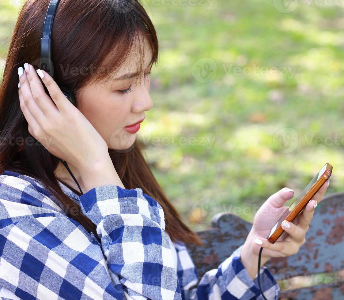 donna asiatica si rilassa con musica sullo smartphone felicemente nel parco foto