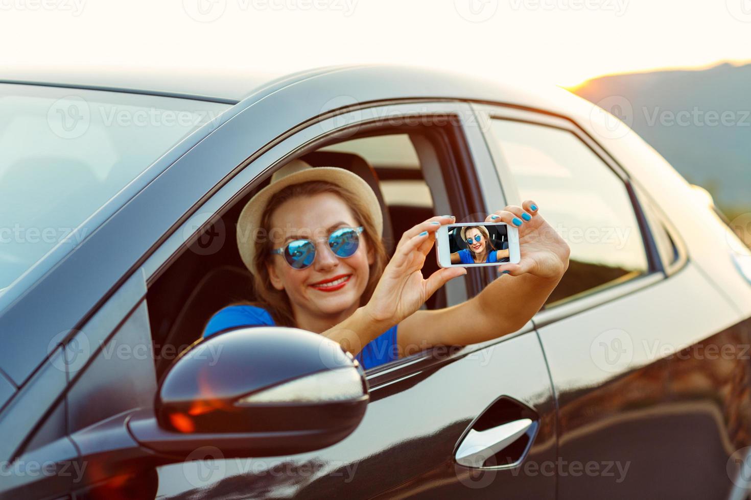 giovane contento donna nel cappello e occhiali da sole fabbricazione se stesso ritratto seduta nel il auto foto