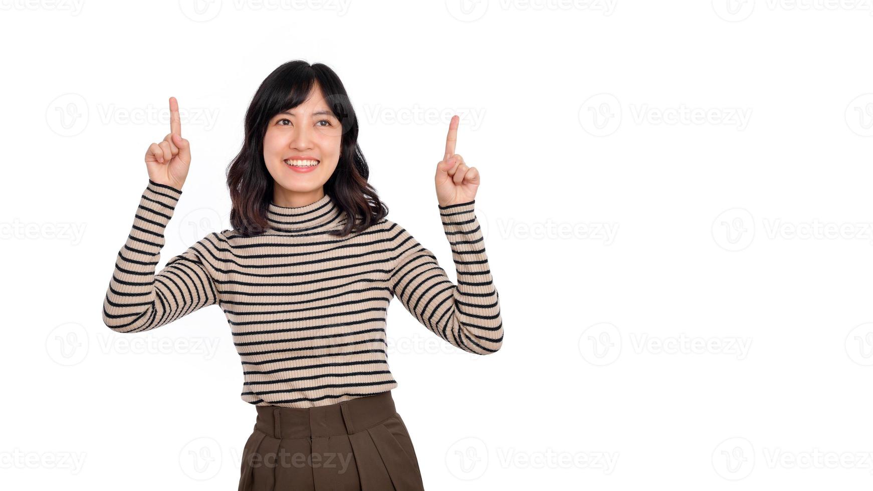bellissimo giovane asiatico donna su maglione stoffa puntamento dita su e guardare a telecamera con Sorridi viso e contento. clic su collegamento sopra gesto su bianca sfondo foto
