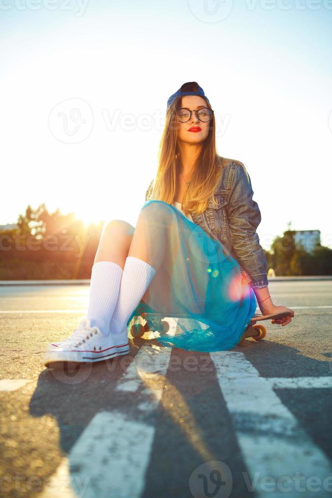all'aperto moda avvicinamento estate ritratto di bella giovane donna in posa con skateboard nel urbano gioventù stile nel cittadina. estate sera luce del sole foto