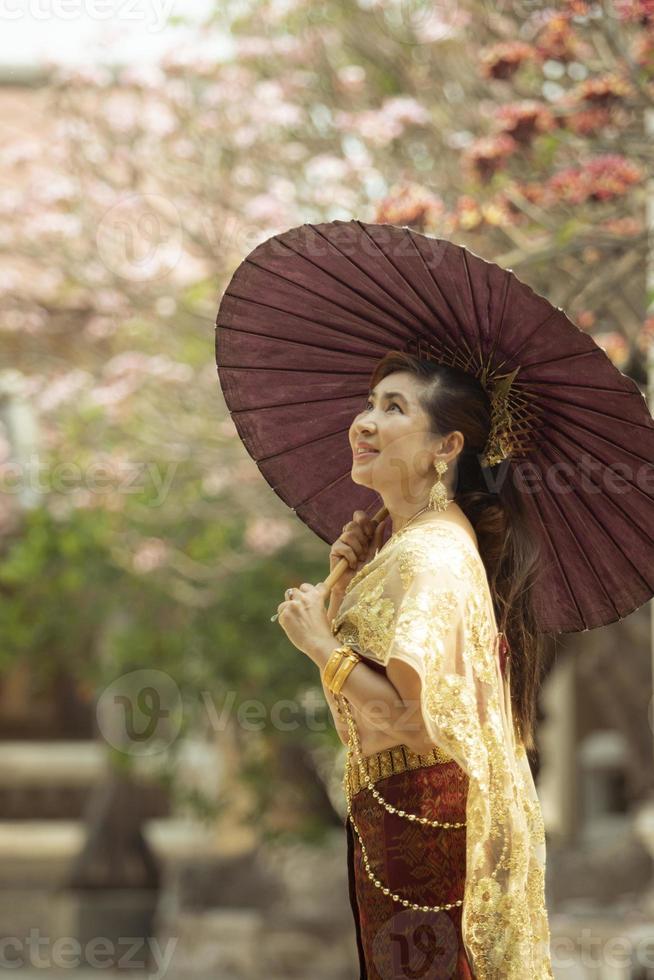 asiatico donna Tenere bambù ombrello in piedi contro plumeria fiore fioritura nel vecchio tempio ayutthaya Tailandia foto