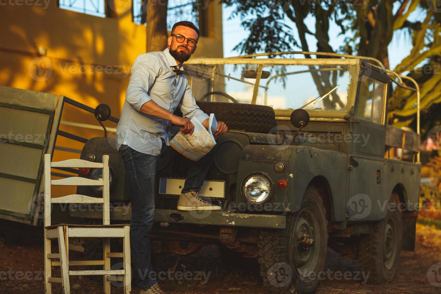 giovane elegante uomo con bicchieri e arco cravatta vedere il carta geografica vicino il vecchio stile suv foto