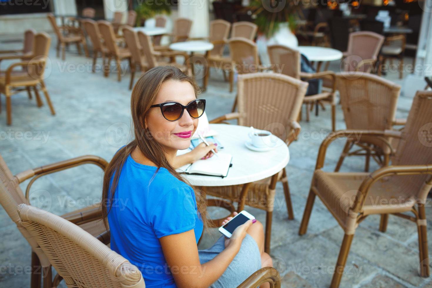 giovane bella moderno blogger utilizzando smartphone e fa Appunti nel un' taccuino nel un' bar foto