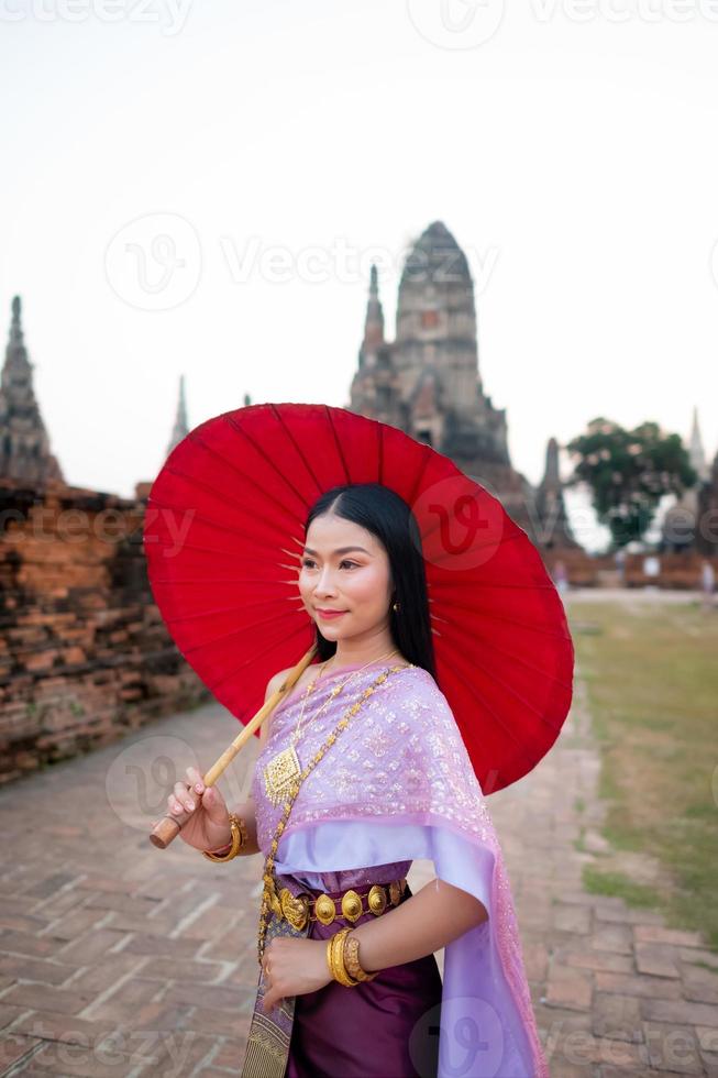 bellissimo tailandese ragazza nel tradizionale vestito costume rosso ombrello come tailandese tempio dove è il pubblico posto, tailandese donna nel tradizionale costume di Tailandia. foto