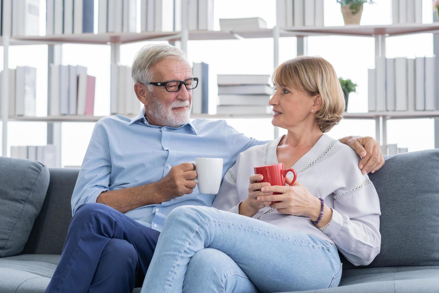 contento mattina, caucasici anziano amante coppia famiglia. maturo, adulto pensionato uomo, donna potabile caffè, tè insieme, abbracciando, abbracciare su divano, divano a casa. piacere marito e moglie stile di vita. foto