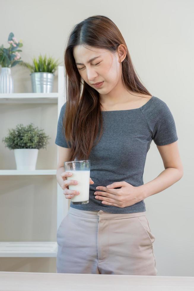 dolore, allergia asiatico giovane donna, ragazza mano nel pancia soffrire dopo bevanda bicchiere di latte, soffrire e cattivo stomaco dolore. lattosio intolleranza e latteria cibo , Salute problema concetto. foto