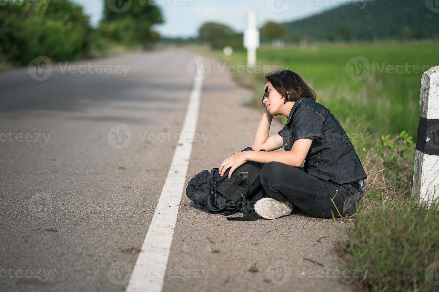 donna sedersi con zaino autostop lungo un' strada nel campagna foto