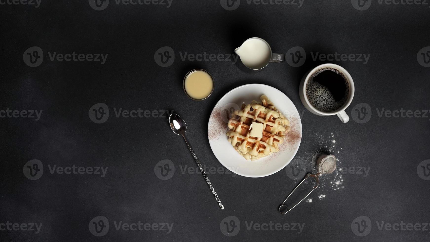 superiore Visualizza di gustoso cialde piatto, caramello salsa, caffè tazza, latte, cucchiaio da dessert, filtro su un' nero calcestruzzo sfondo foto