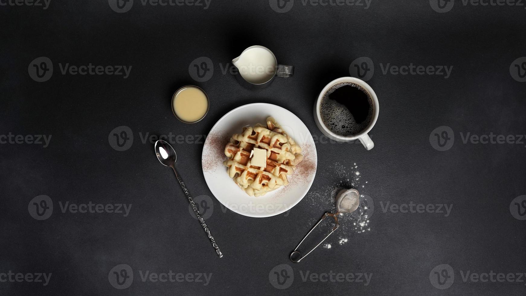 superiore Visualizza di gustoso cialde piatto, caramello salsa, caffè tazza, latte, cucchiaio da dessert, filtro su un' nero calcestruzzo sfondo foto